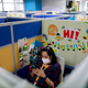 A tutor wearing a face mask sits in a cubicle decorated with images of brightly colored monkeys swinging from vines